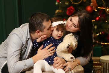 a man and a woman holding a baby and a teddy bear