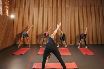 Yoga class with diverse adults stretching on mats in a cozy wooden studio.